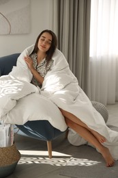 Photo of Beautiful young woman wrapped with soft blanket relaxing on armchair at home