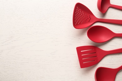 Photo of Set of red cooking utensils on white wooden table, flat lay. Space for text