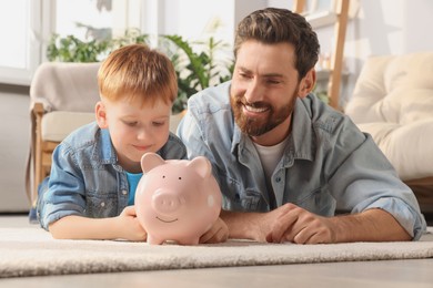 Photo of Father and his son with ceramic piggy bank on floor at home