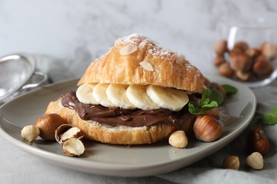 Delicious croissant with banana, chocolate and hazelnuts on gray table, closeup