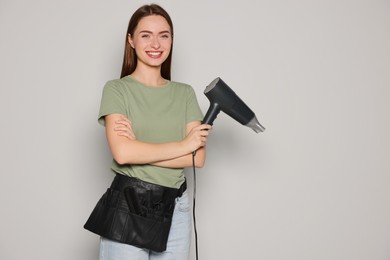 Photo of Portrait of happy hairdresser with hairdryer on light background. Space for text