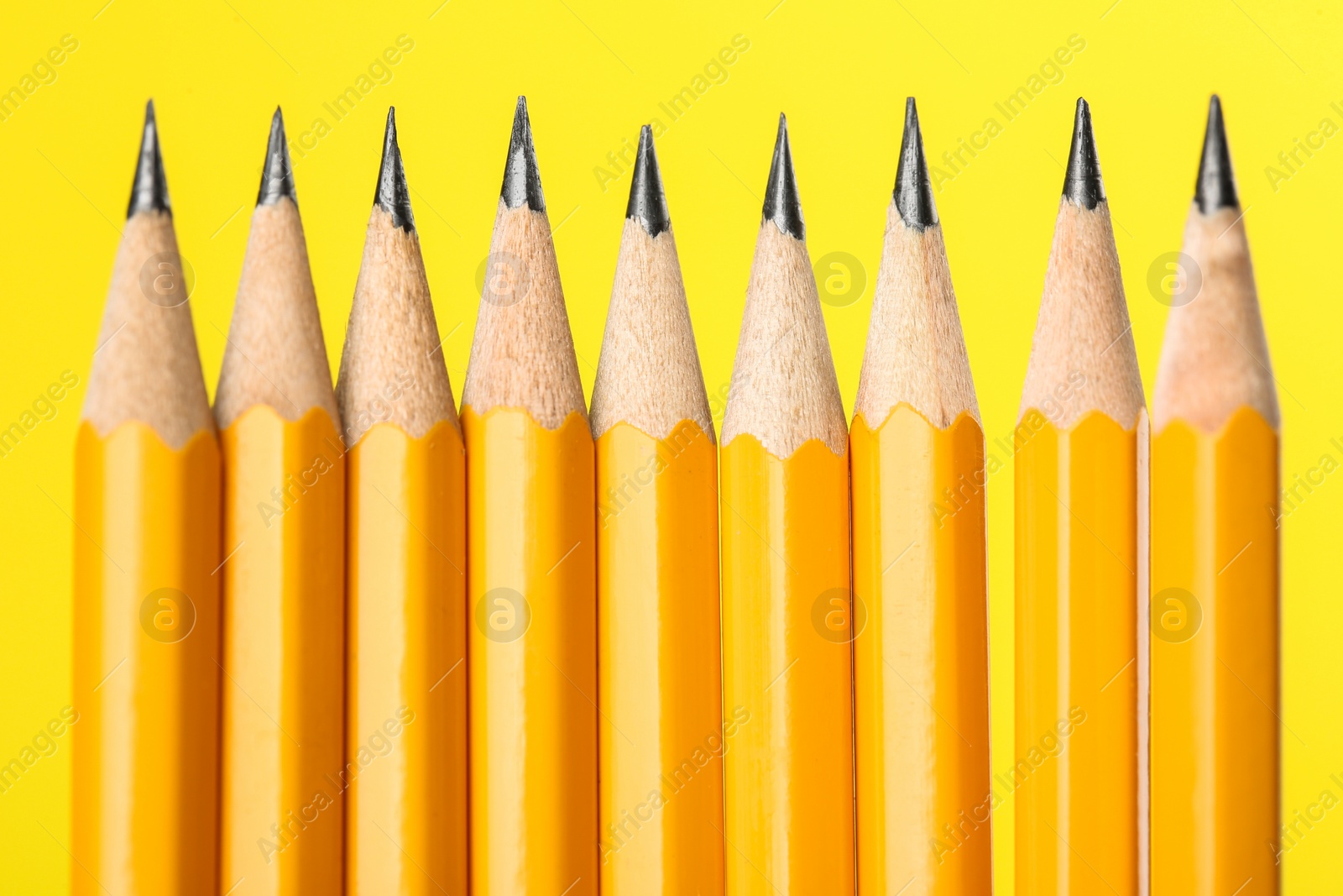 Photo of Many sharp graphite pencils on yellow background, macro view