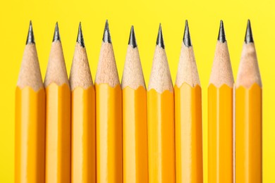 Photo of Many sharp graphite pencils on yellow background, macro view
