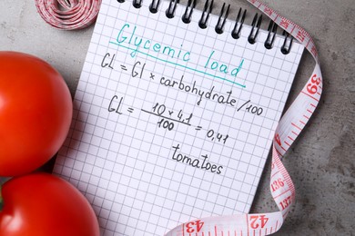 Photo of Notebook with calculated glycemic load for tomatoes, measuring tape and fresh vegetables on grey table, flat lay