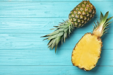 Photo of Fresh whole and cut pineapples on light blue wooden background, top view. Space for text