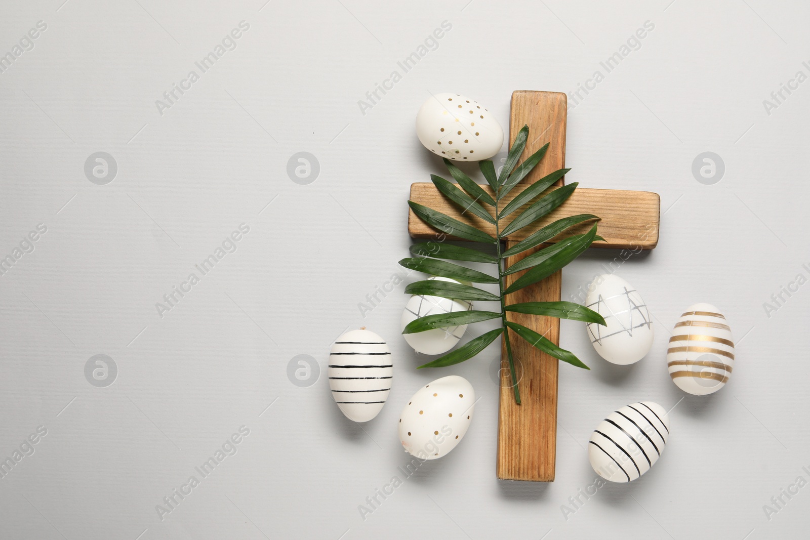 Photo of Wooden cross, painted Easter eggs and palm leaf on light grey background, flat lay. Space for text