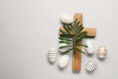 Wooden cross, painted Easter eggs and palm leaf on light grey background, flat lay. Space for text