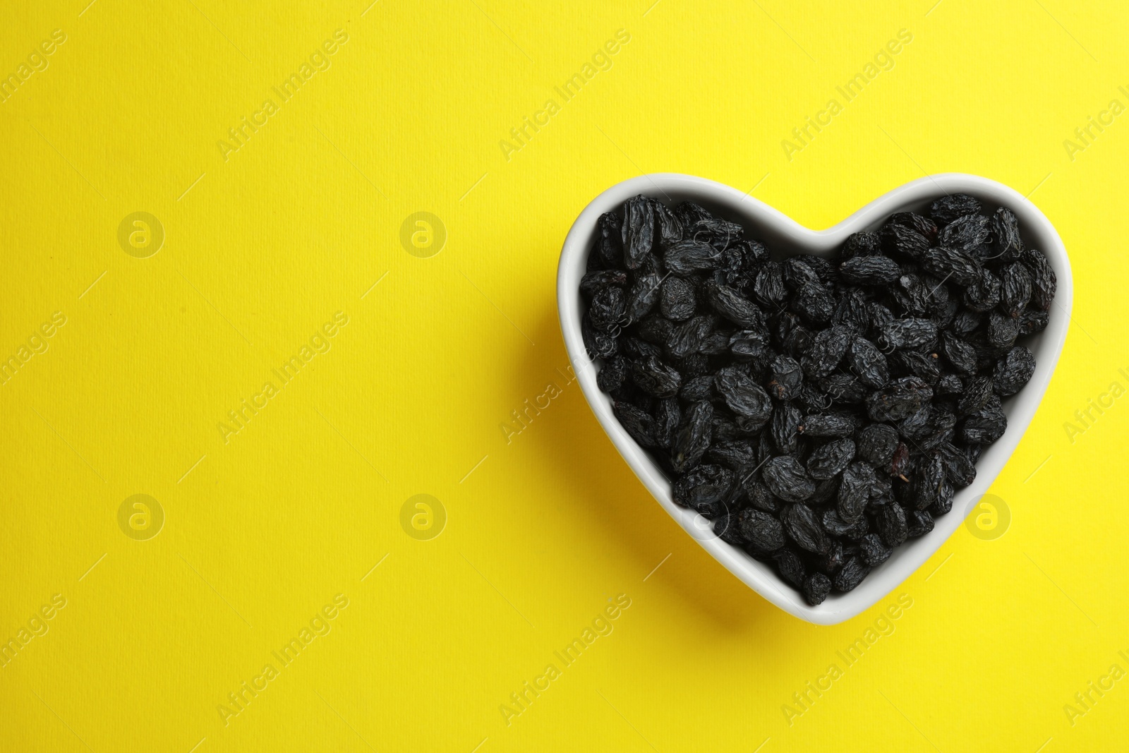 Photo of Heart shaped plate with raisins and space for text on color background, top view. Dried fruit as healthy snack