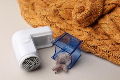 Photo of Modern fabric shaver with fuzz and orange knitted sweater on white background