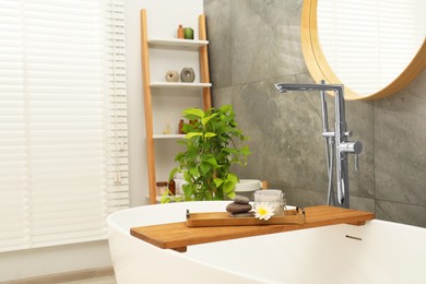 Photo of Shelving unit and wooden tub tray with different spa products in bathroom