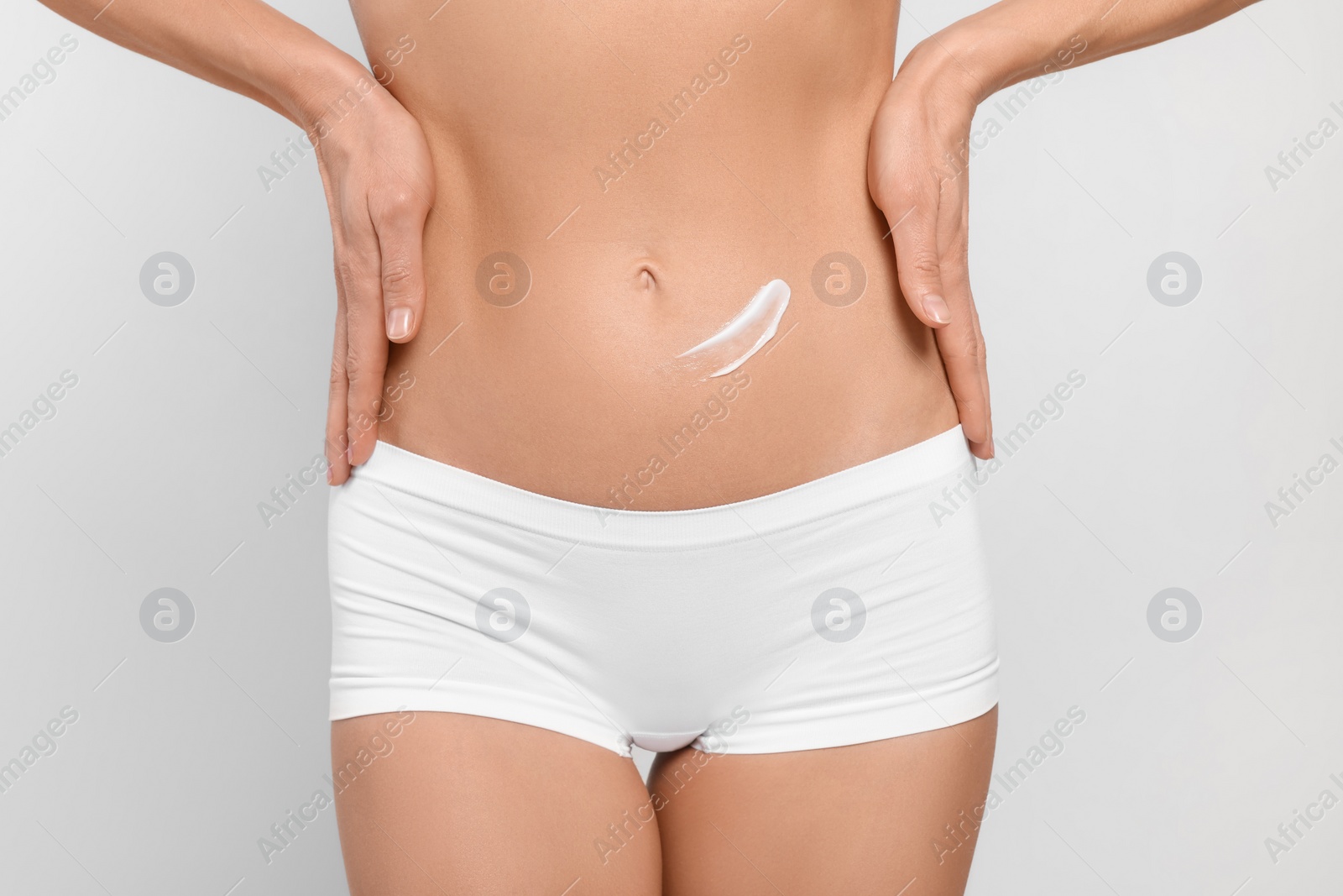 Photo of Woman with body cream onto her belly against white background, closeup