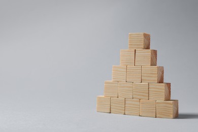 Photo of Pyramid of blank wooden cubes on light grey background. Space for text