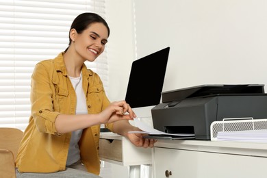 Photo of Woman using modern printer at workplace indoors