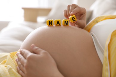 Photo of Pregnant woman with cubes on belly indoors, closeup. Choosing baby name