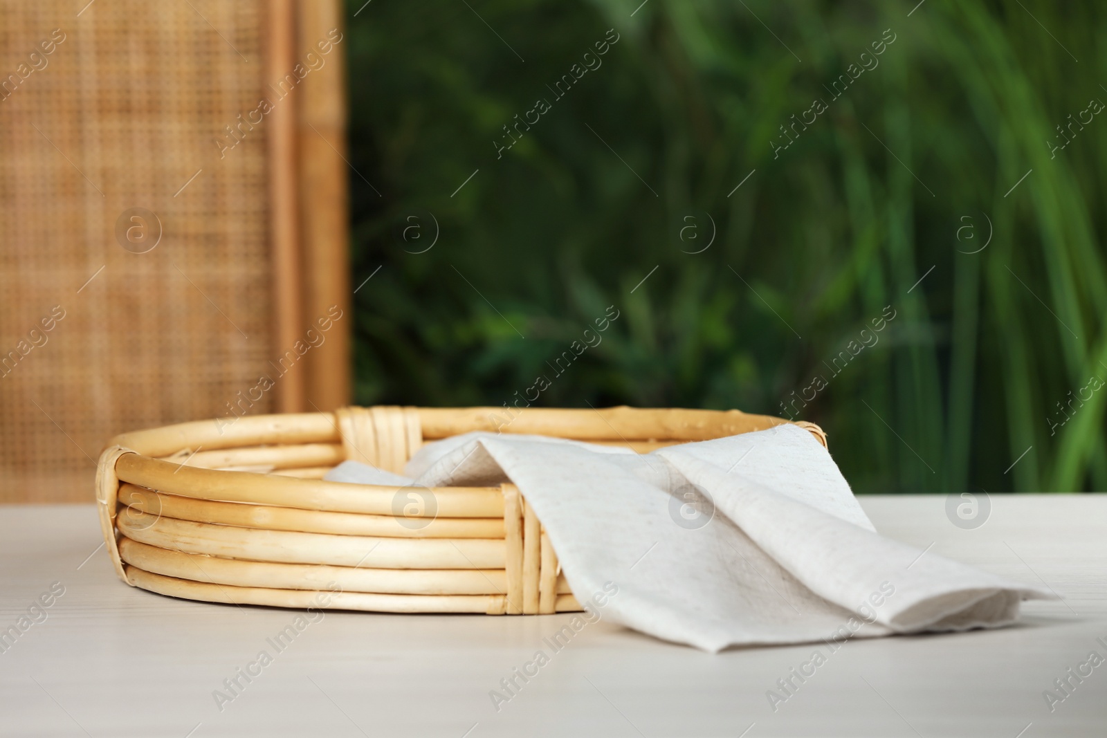 Photo of Stylish wicker tray with cloth on white table against blurred background