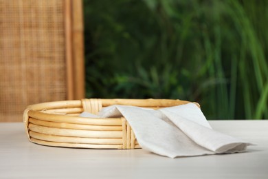 Stylish wicker tray with cloth on white table against blurred background