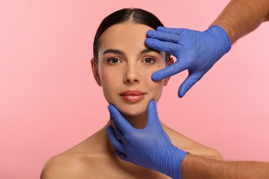 Photo of Doctor checking patient's face before cosmetic surgery operation on pink background