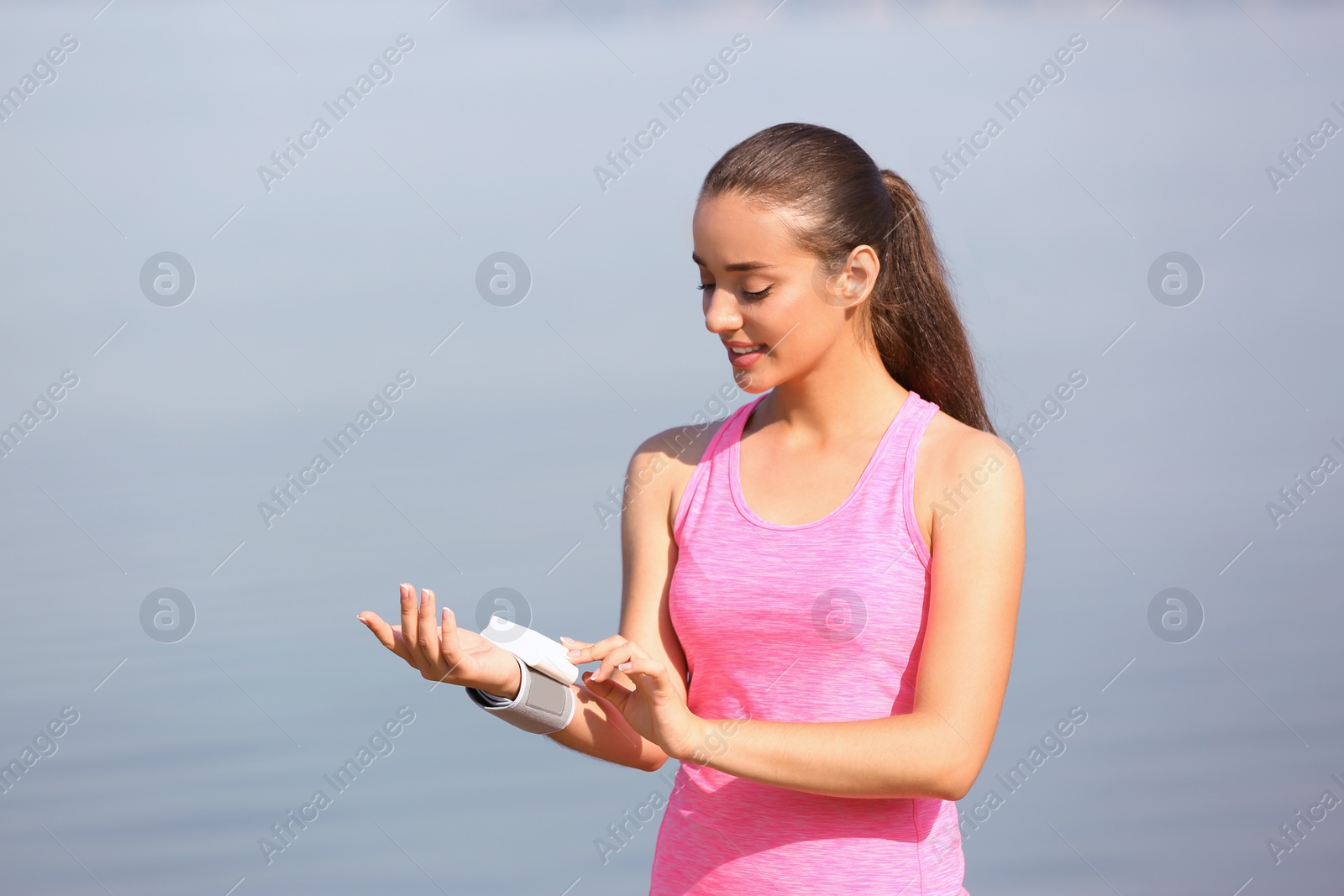 Photo of Young woman checking pulse outdoors on sunny day