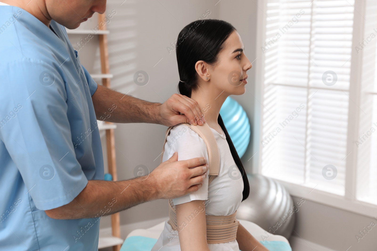 Photo of Orthopedist helping patient to put on posture corrector in clinic, closeup. Scoliosis treatment