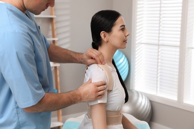 Photo of Orthopedist helping patient to put on posture corrector in clinic, closeup. Scoliosis treatment