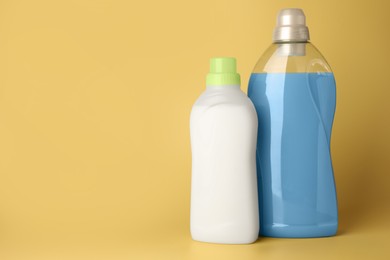 Photo of Bottles of fabric softener on pale yellow background, space for text