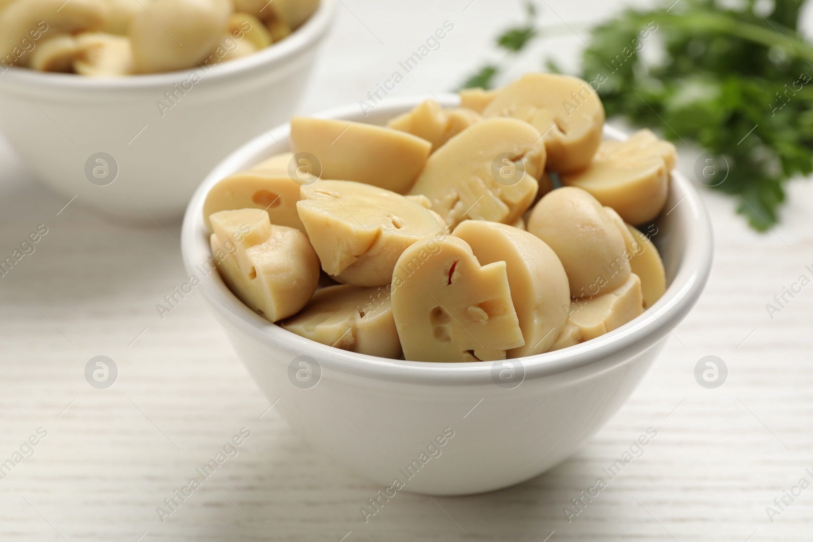 Photo of Delicious marinated mushrooms in bowl on white wooden table, closeup