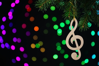 Wooden music note hanging on Christmas tree on black background with blurred lights. Space for text