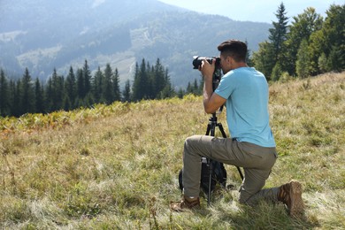 Man taking photo of mountain landscape with modern camera on tripod outdoors