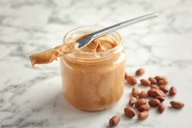 Photo of Jar and knife with creamy peanut butter on table