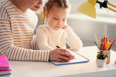 Photo of Woman helping her daughter with homework at table indoors