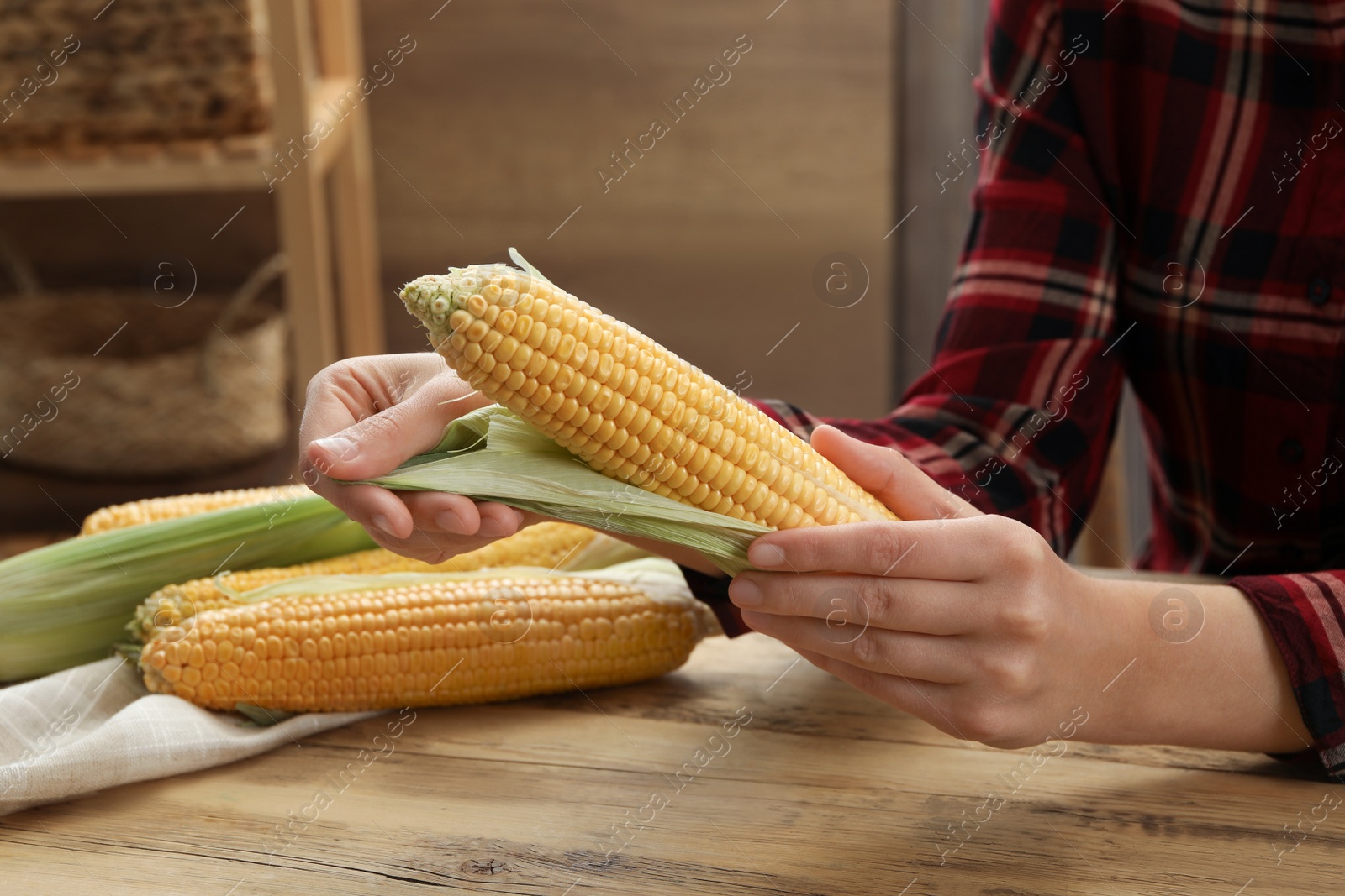 Photo of Woman husking corn cob at wooden table, closeup