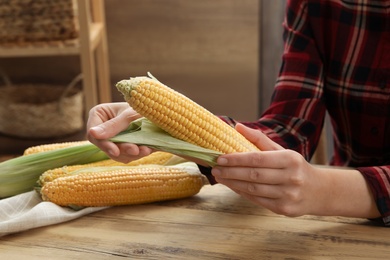 Woman husking corn cob at wooden table, closeup