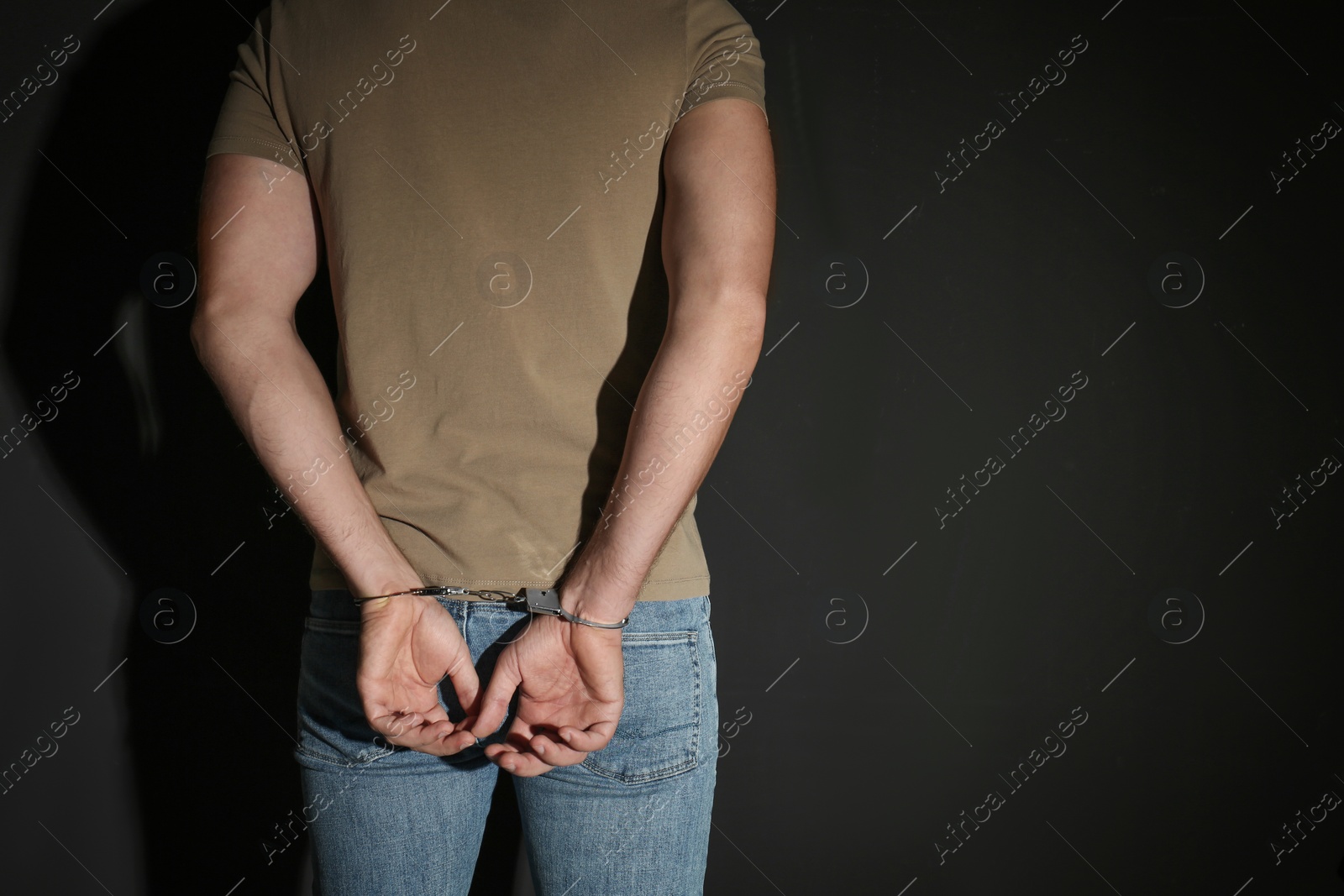 Photo of Male criminal in handcuffs near black wall, closeup