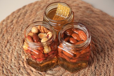 Photo of Jars with different nuts and honey on wicker mat, closeup