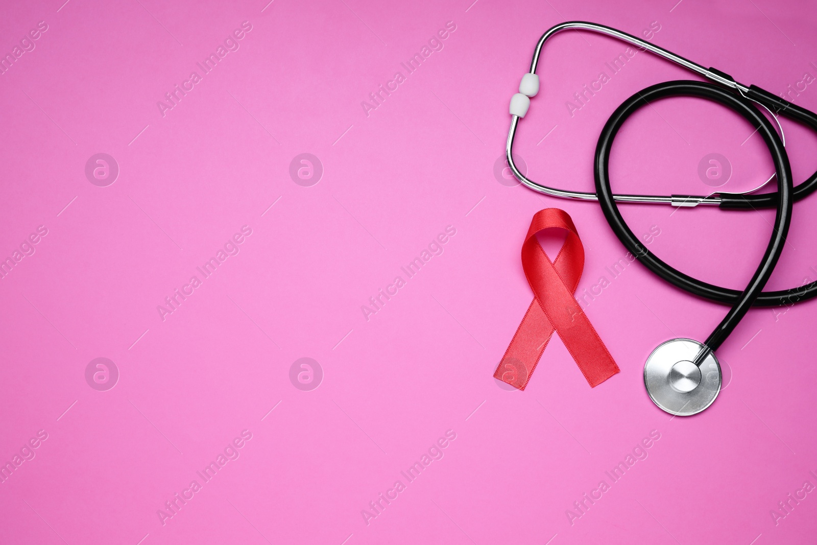 Photo of Red ribbon and stethoscope on pink background, flat lay with space for text. AIDS disease awareness