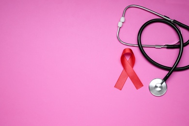 Red ribbon and stethoscope on pink background, flat lay with space for text. AIDS disease awareness