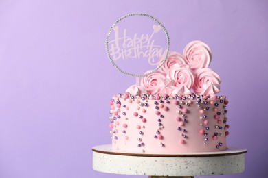 Photo of Beautifully decorated birthday cake on stand against violet background, space for text