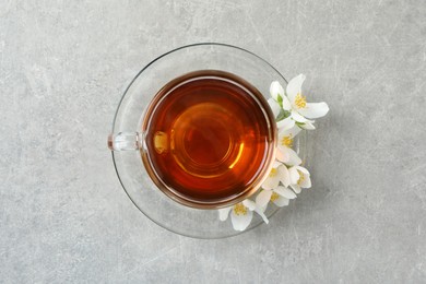 Photo of Glass cup of aromatic jasmine tea and fresh flowers on grey table, top view