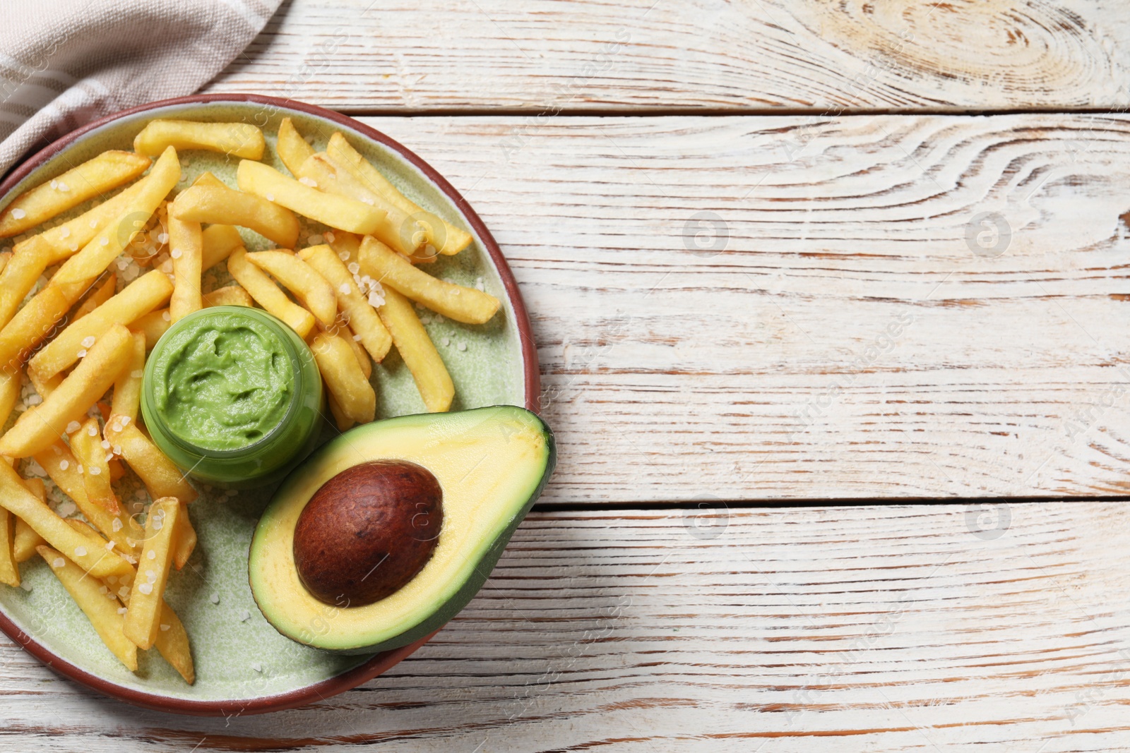 Photo of Plate with french fries, guacamole dip and avocado served on white wooden table, top view. Space for text