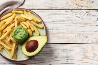 Plate with french fries, guacamole dip and avocado served on white wooden table, top view. Space for text