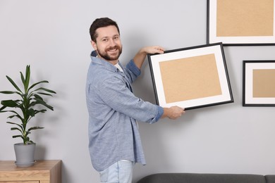 Man hanging picture frame on gray wall at home