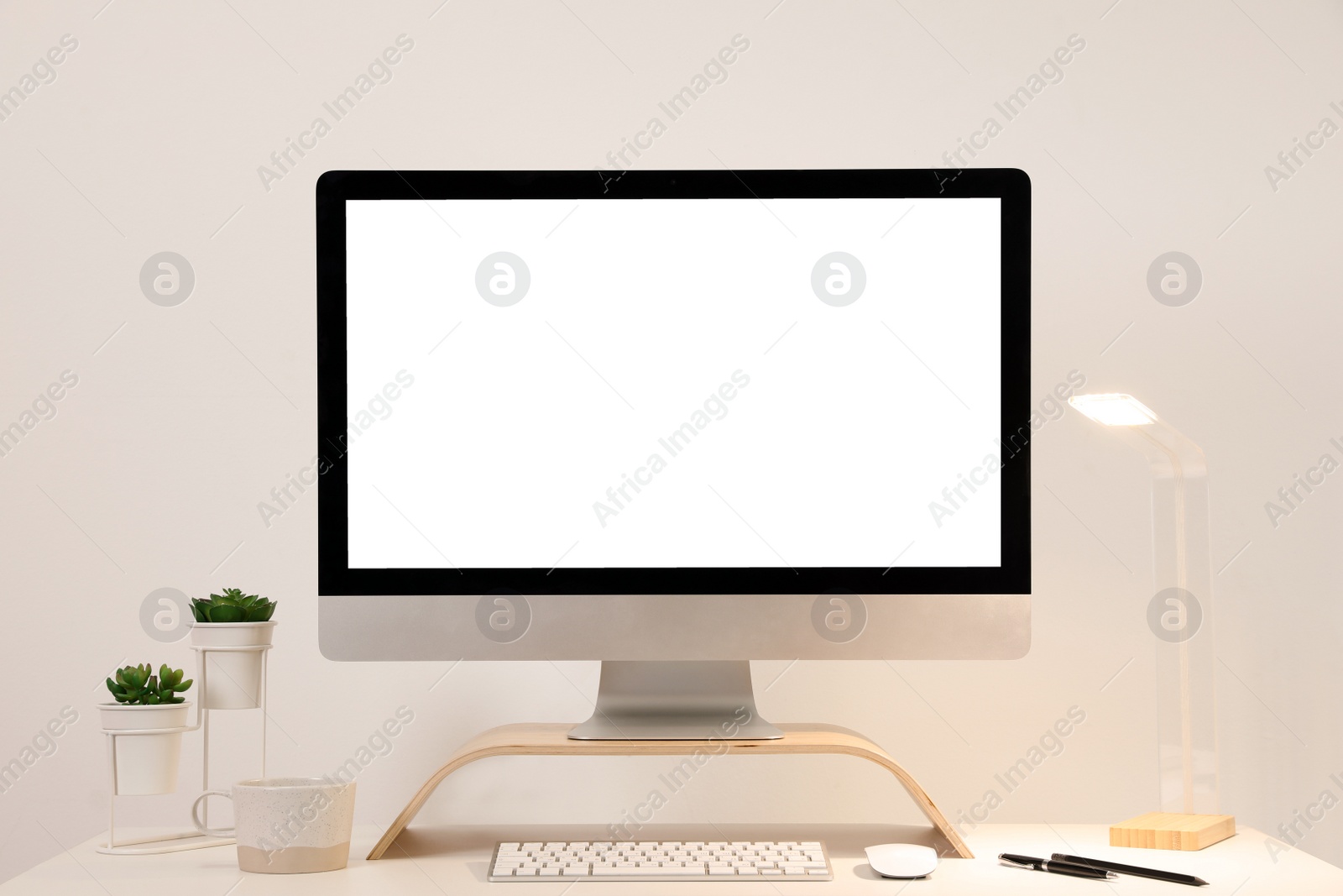 Photo of Comfortable workplace with blank computer display on desk near light wall. Space for text