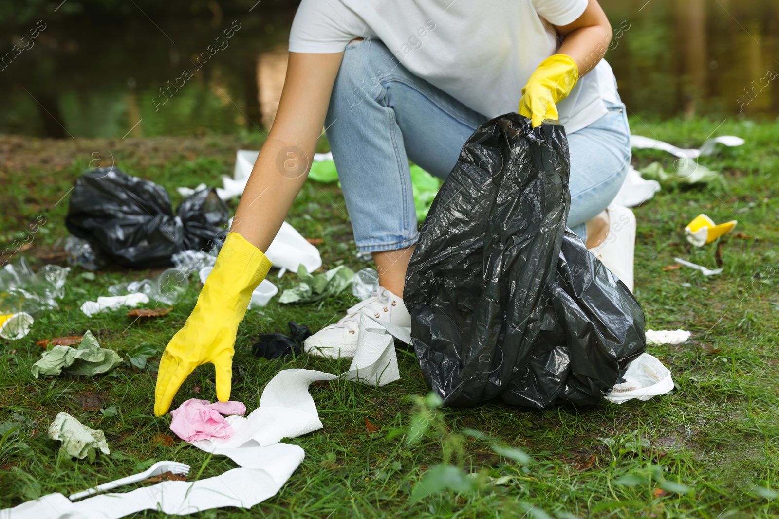 Photo of Woman with plastic bag collecting garbage in park, closeup