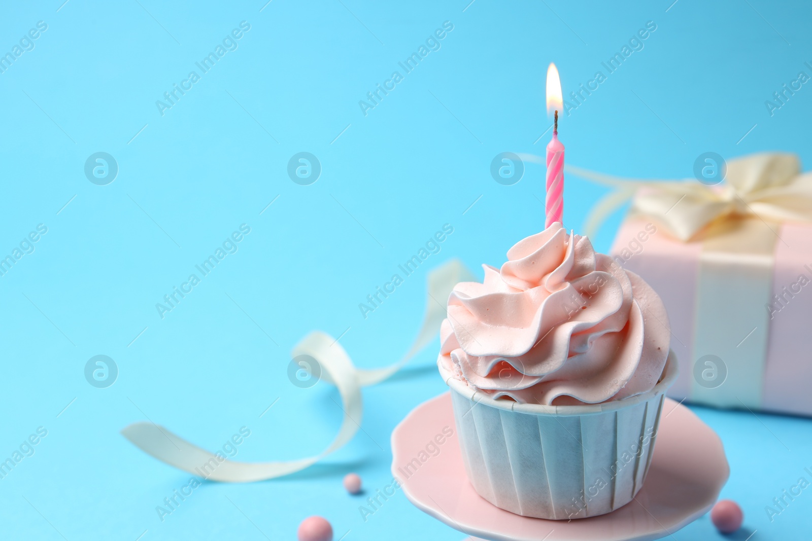 Photo of Delicious birthday cupcake with burning candle on light blue background, closeup. Space for text