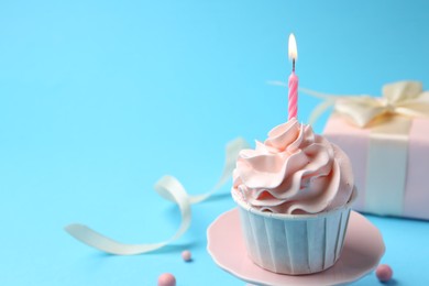 Delicious birthday cupcake with burning candle on light blue background, closeup. Space for text