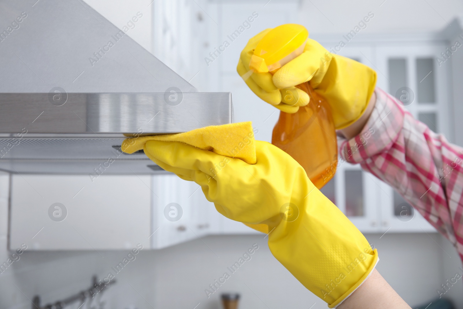 Photo of Woman cleaning kitchen hood with rag and detergent indoors, closeup
