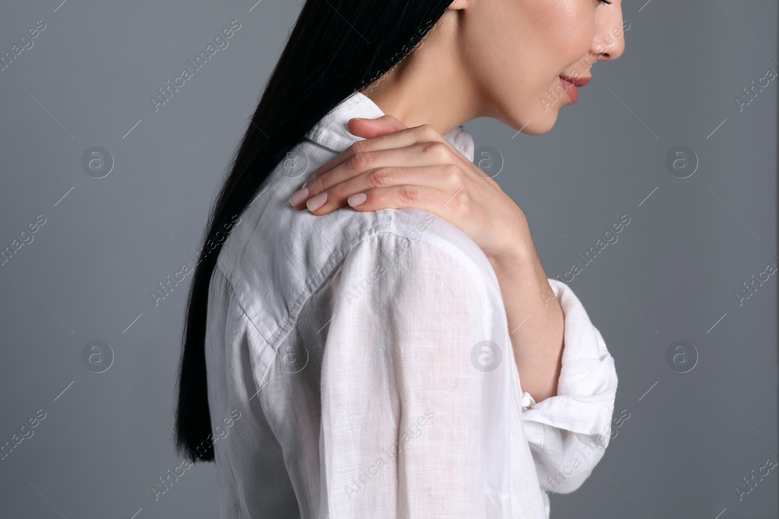 Photo of Woman suffering from shoulder pain on grey background, closeup