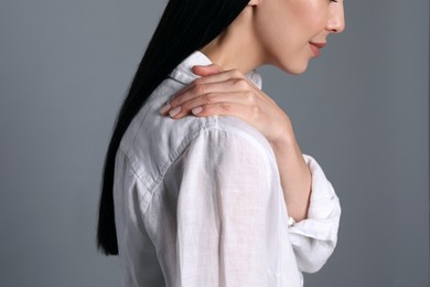 Photo of Woman suffering from shoulder pain on grey background, closeup