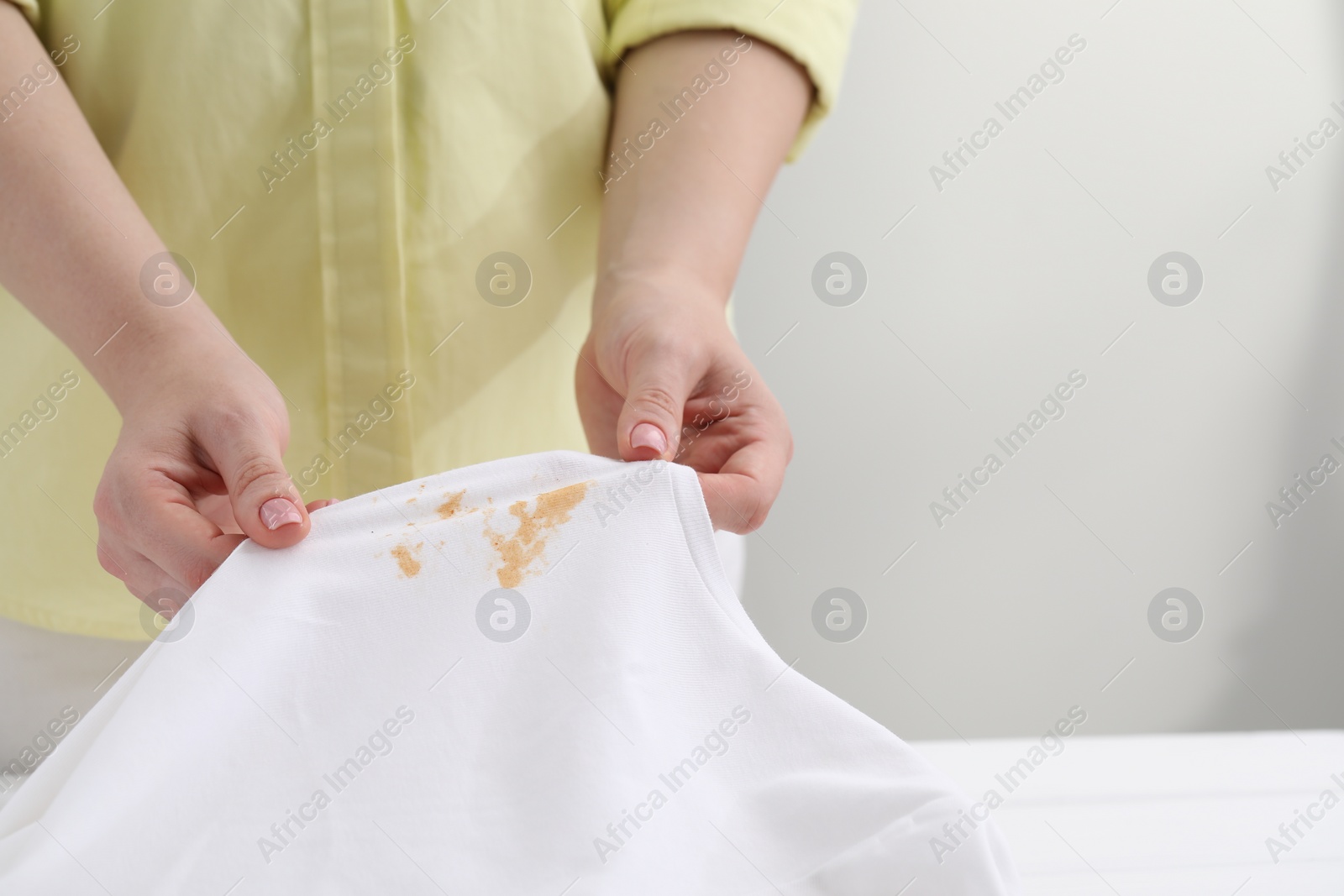 Photo of Woman holding shirt with stain at white table against light background, closeup. Space for text