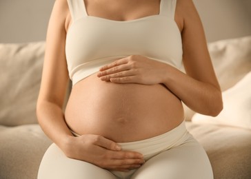 Photo of Pregnant woman touching her belly indoors, closeup